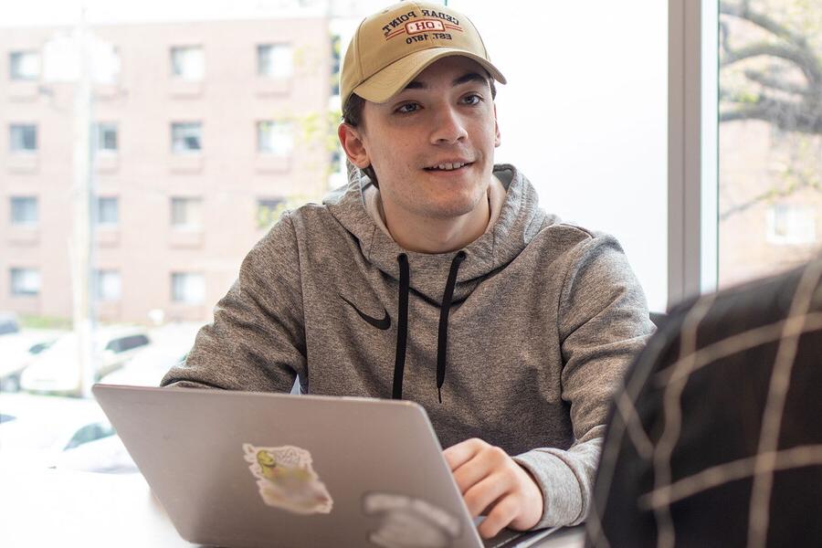 Young man sitting with a laptop in front of a window.